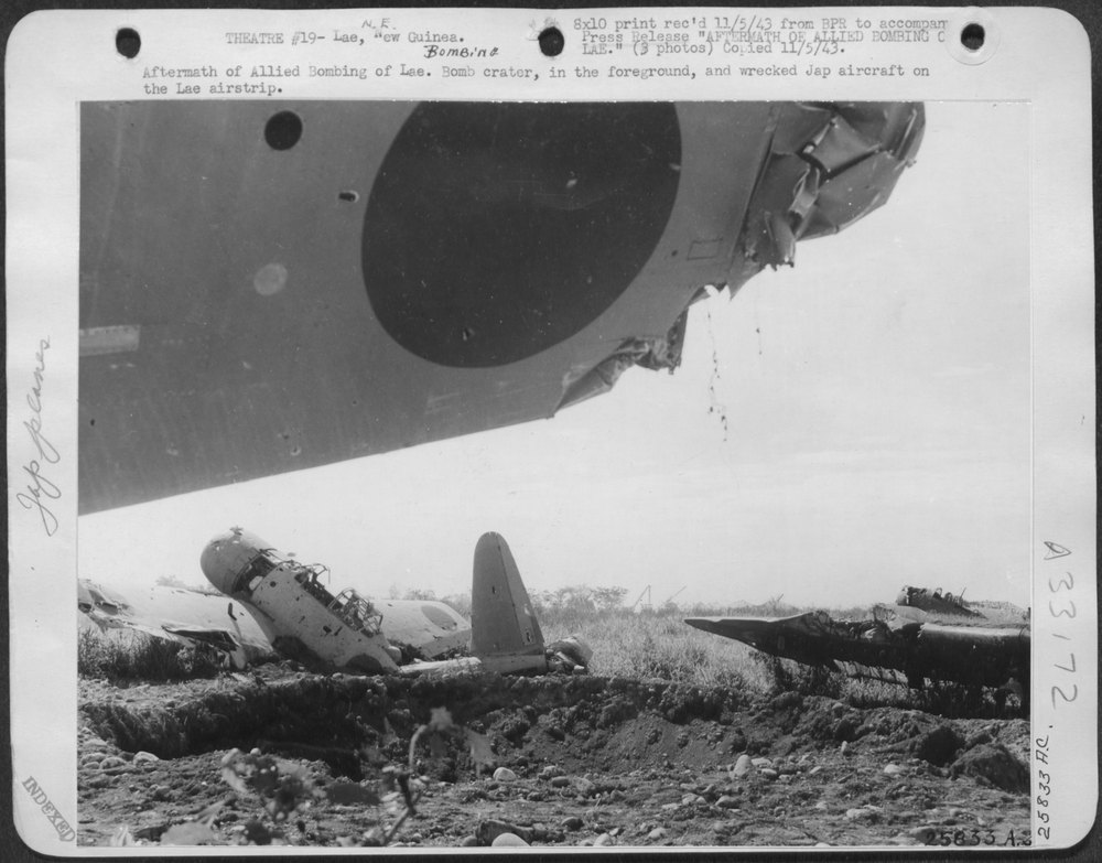 Bomb crater, in the foreground, and wrecked Jap aircraft on the Lae