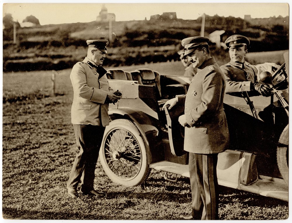 Three men in military uniforms with an open-top automobile